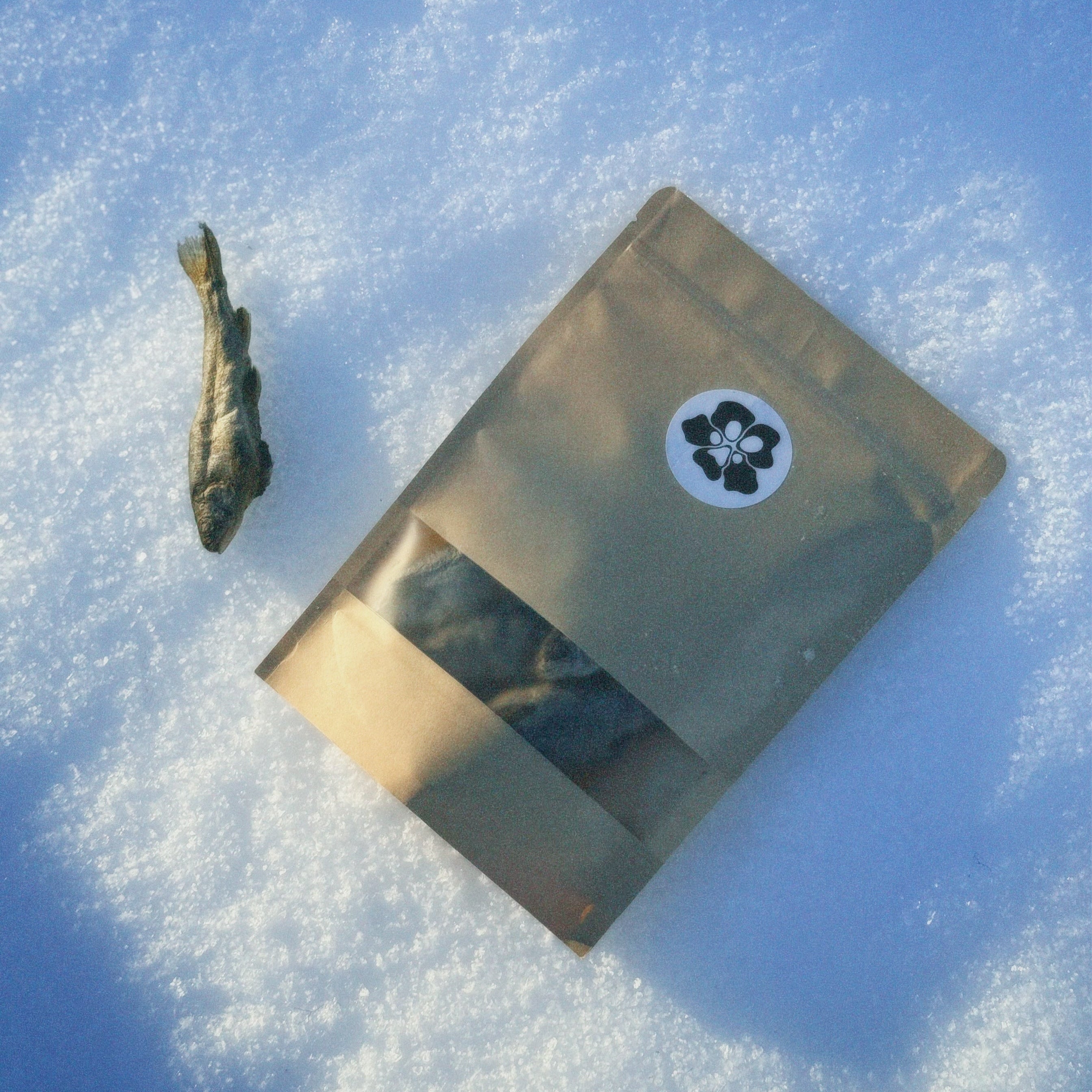 Gold-colored package with a black and white treatosbox logo on a snowy surface and a rainbow trout